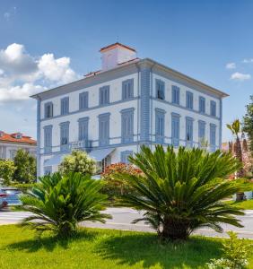 een groot wit gebouw met palmbomen ervoor bij Hotel Tirreno in Marina di Massa