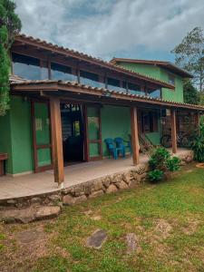 a green house with blue chairs on the porch at Pousada Aurora in Praia do Rosa