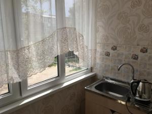 een keuken met een wastafel en een raam met gordijnen bij Квартира в городке Бостери in Bosteri