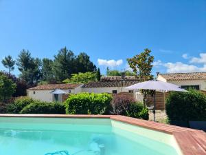 uma piscina com um guarda-sol e uma casa em MAS GABELYS au pied de la Sainte Victoire, rez de jardin avec terrasse et piscine em Trets