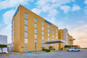 un hotel amarillo con una furgoneta blanca estacionada frente a él en City Express by Marriott Culiacan en Culiacán