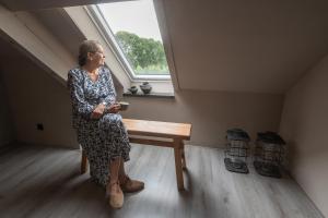 a woman sitting on a bench in a room with a window at Landelijke boerderijkamer, dichtbij Kinderdijk in Oud-Alblas
