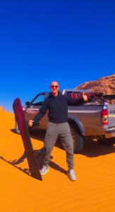 a man standing in front of a truck with a snowboard at Adel rum camp bubbles in Wadi Rum