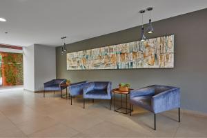 een wachtkamer met blauwe stoelen en een schilderij aan de muur bij City Express by Marriott Puebla Centro in Puebla