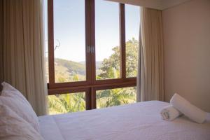 a bedroom with a large window with a white bed and a view at Flat 333 - Luxo e Vista da Pedra Azul in Pedra Azul
