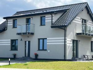 a white house with a black roof at Apartamenty Pod Jodłami in Sarbinowo