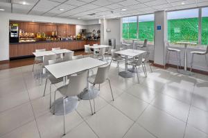 a cafeteria with white tables and chairs and a kitchen at City Express by Marriott Aguascalientes Sur in Aguascalientes