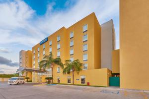 un hotel amarillo con palmeras en un aparcamiento en City Express by Marriott Mazatlan en Mazatlán