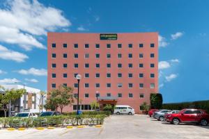 a large red brick building with cars parked in a parking lot at City Express Junior by Marriott Merida Altabrisa in Mérida