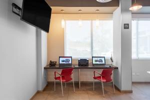 una oficina con 2 ordenadores en un escritorio con sillas rojas en City Express Junior by Marriott Merida Altabrisa, en Mérida