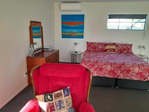 a bedroom with a bed with a red bedspread and a chair at Moana Vista in One Tree Point