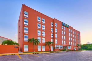 a large red building with palm trees in a parking lot at City Express Junior by Marriott Cancun in Cancún