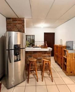 a kitchen with a stainless steel refrigerator and wooden stools at Casa Tierra Viva in Managua