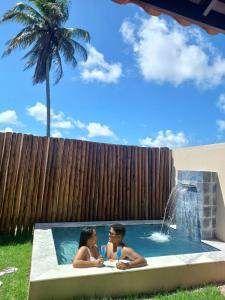 Due persone sedute in una piscina con una fontana di Marinho Suítes Milagres a São Miguel dos Milagres