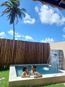 two people sitting in a pool with a fountain at Marinho Suítes Milagres in São Miguel dos Milagres