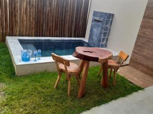 een houten tafel en 2 stoelen naast een zwembad bij Marinho Suítes Milagres in São Miguel dos Milagres