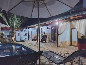 a swimming pool with an umbrella and two chairs at Pousada Love Piri in Pirenópolis