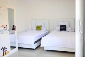 a white bedroom with two beds and a mirror at Urbanview Hotel Eropa Maros Near Sultan Hasanuddin Airport in Maros