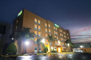 a hotel with palm trees in front of a building at City Express Junior by Marriott Toluca Aeropuerto in Toluca