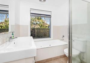 ein weißes Bad mit einem Waschbecken, einem WC und einem Fenster in der Unterkunft Cookes Haven in Gerringong