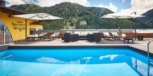 a swimming pool with chairs and umbrellas on a building at Boutique Appartements in Saalbach Hinterglemm