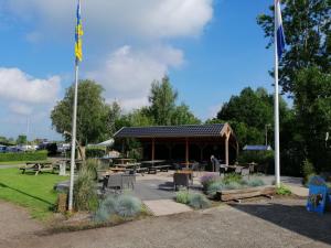 a pavilion with picnic tables and benches in a park at Camping Kleine Belterwijde, Wiede Lodge met uitzicht over het water in Belt-Schutsloot
