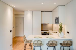 波尔图Blissful Suites Porto by gaiarooms的一个带白色橱柜的厨房和一个带椅子的岛屿