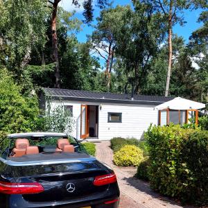 een auto geparkeerd voor een wit huis bij Heerlijk chalet in prachtige natuur. in Doornspijk