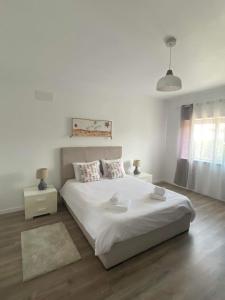 a white bedroom with a large bed and two tables at Casa do coral in Peniche