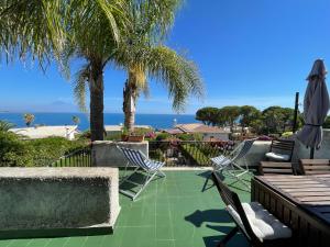 patio z krzesłami, palmami i oceanem w obiekcie Villa Baia del Riccio w mieście Agnone Bagni