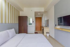 1 dormitorio con 1 cama blanca grande y TV en RedLiving Apartemen Evenciio - Arutala Living en Pondokcina