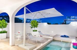 uma piscina com um guarda-sol branco e cadeiras e uma mesa em Pazziella Garden & Suites em Capri