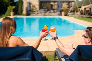 a man and woman holding drinks in front of a pool at Les Dépendances du Château Chapeau Cornu in Vignieu