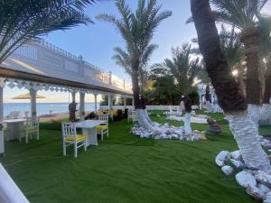 Lidia Dahab Hotel and Restaurant في دهب: وجود حديقة على الشاطئ بها طاولات والنخيل
