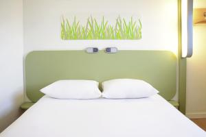 a bed with two white pillows and a painting on the wall at ibis Budget Courbevoie Paris La Défense in Courbevoie