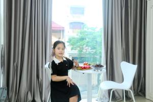 ein junges Mädchen auf einem Stuhl vor einem Tisch in der Unterkunft Noi Bai Ville Airport Hotel in Hanoi