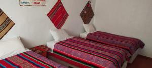2 camas en una habitación con mantas rojas y coloridas en TITIKAKA NATURAL LODGE - LUQUINA en Chucuito