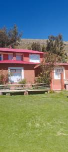 una casa roja con un campo verde delante de ella en TITIKAKA NATURAL LODGE - LUQUINA en Chucuito