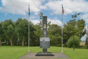 un monument dans un champ arborant deux drapeaux dans l'établissement Le Cotentin - Joli appt 2 chambres à Carentan, à Auvers