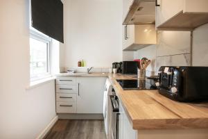 a kitchen with white cabinets and a wooden counter top at Spacious 2 BR Apartments - 5 mins from QMC, Universities and City Centre! in Nottingham