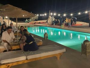Agafay, La Ferme Nomade Bivouac في El Karia: مجموعة من الناس يجلسون حول طاولة بجانب مسبح