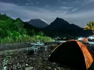 a tent and a table in a river with mountains at Rainbow Lodge Tambatuon in Kota Belud