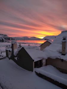 a house covered in snow with a sunset in the background at Cerro Pirámide Alojamiento in Caviahue