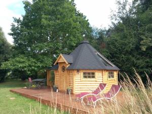 Cabaña de madera con techo negro y 2 sillas en Insolite: Le Kota du Lutin Many, en Saint-Christophe-sur-Condé