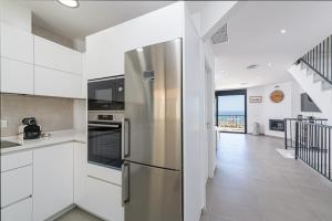 トレ・デ・ベナガルボンにあるWintowinRentals New and Sea Viewのキッチン(白いキャビネット、ステンレス製の冷蔵庫付)