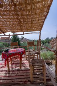 two chairs and a table on a patio with a thatch roof at Agafay, La Ferme Nomade Bivouac in El Karia