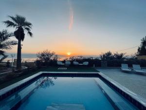 a swimming pool with a sunset in the background at The Precious Villa in Sowayma