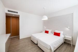 a white bedroom with two white beds and red pillows at AlvorMar Apartamentos Turisticos in Alvor