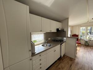 a kitchen with white cabinets and a sink and a refrigerator at ZP 470 - Camping de Zandput in Vrouwenpolder