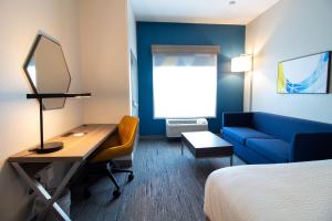 Habitación de hotel con escritorio, cama y sofá azul en Holiday Inn Express Leland - Wilmington Area, an IHG Hotel, en Leland